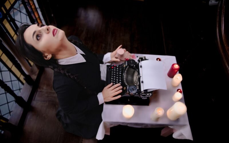 A woman in a vintage outfit types on a typewriter surrounded by candles in a gothic setting.