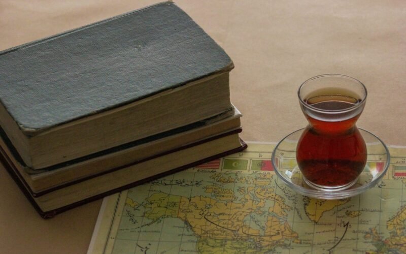 Stack of books, a world map, and a tea glass evoke a warm reading atmosphere.