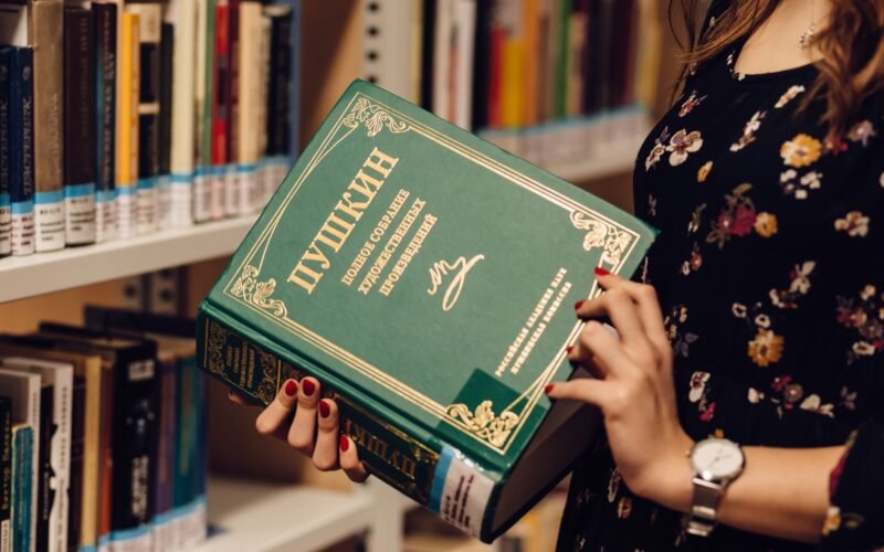 A woman holds a Russian literature book in a library, showcasing a focused study environment.