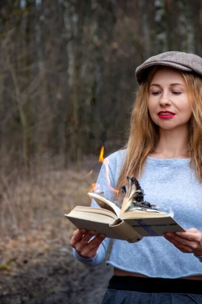 Woman reading a burning book in a forest shows dramatic tension and mystery.