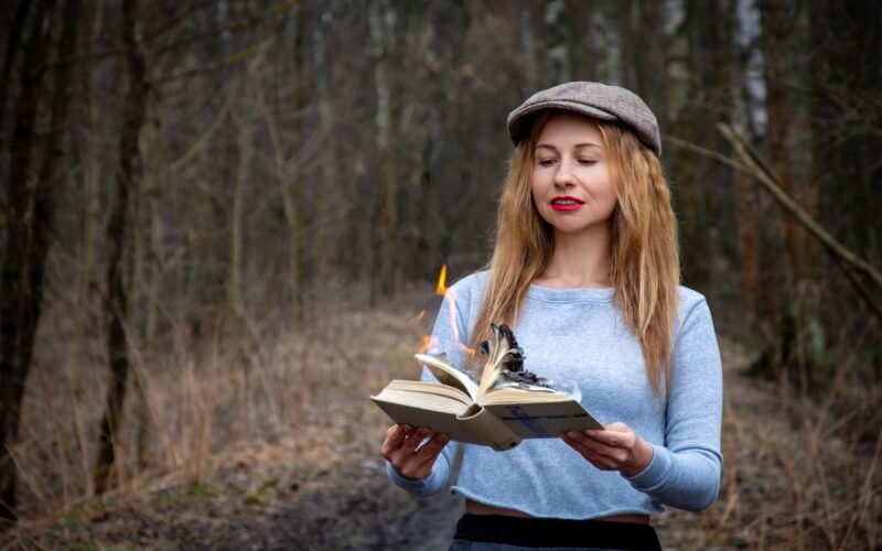 Woman reading a burning book in a forest shows dramatic tension and mystery.