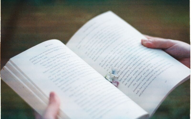 Hands holding an open book with blurred text, creating an intimate reading atmosphere.