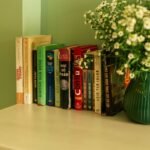 A cozy bookshelf with various books next to a flower vase in a calm setting.