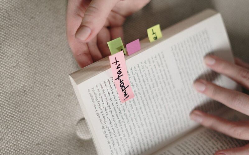 Hands holding a book with colorful sticky notes marking important pages.