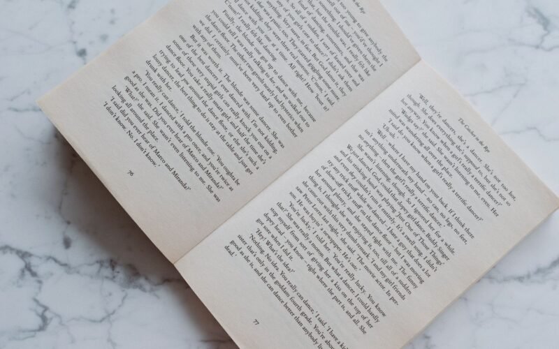 Top view of opened fiction book in soft binding lying on marble table