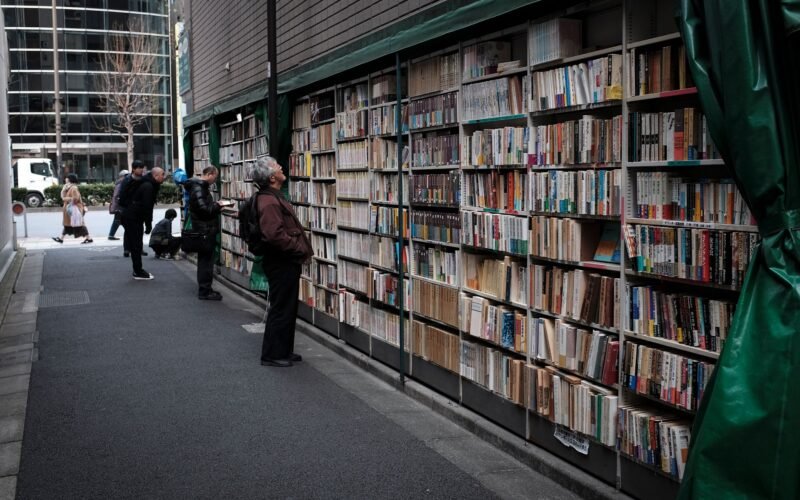 Outdoor bookshelves in Tokyo with people exploring literature on a city street.