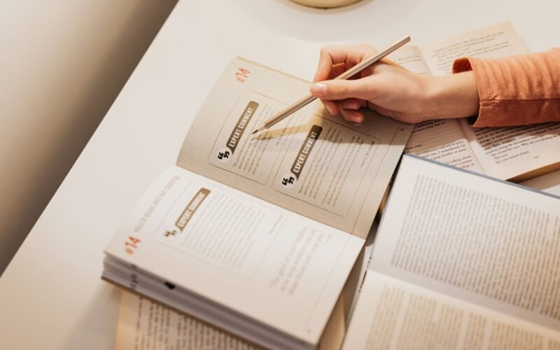 A woman using a pencil to annotate books while studying at a desk.